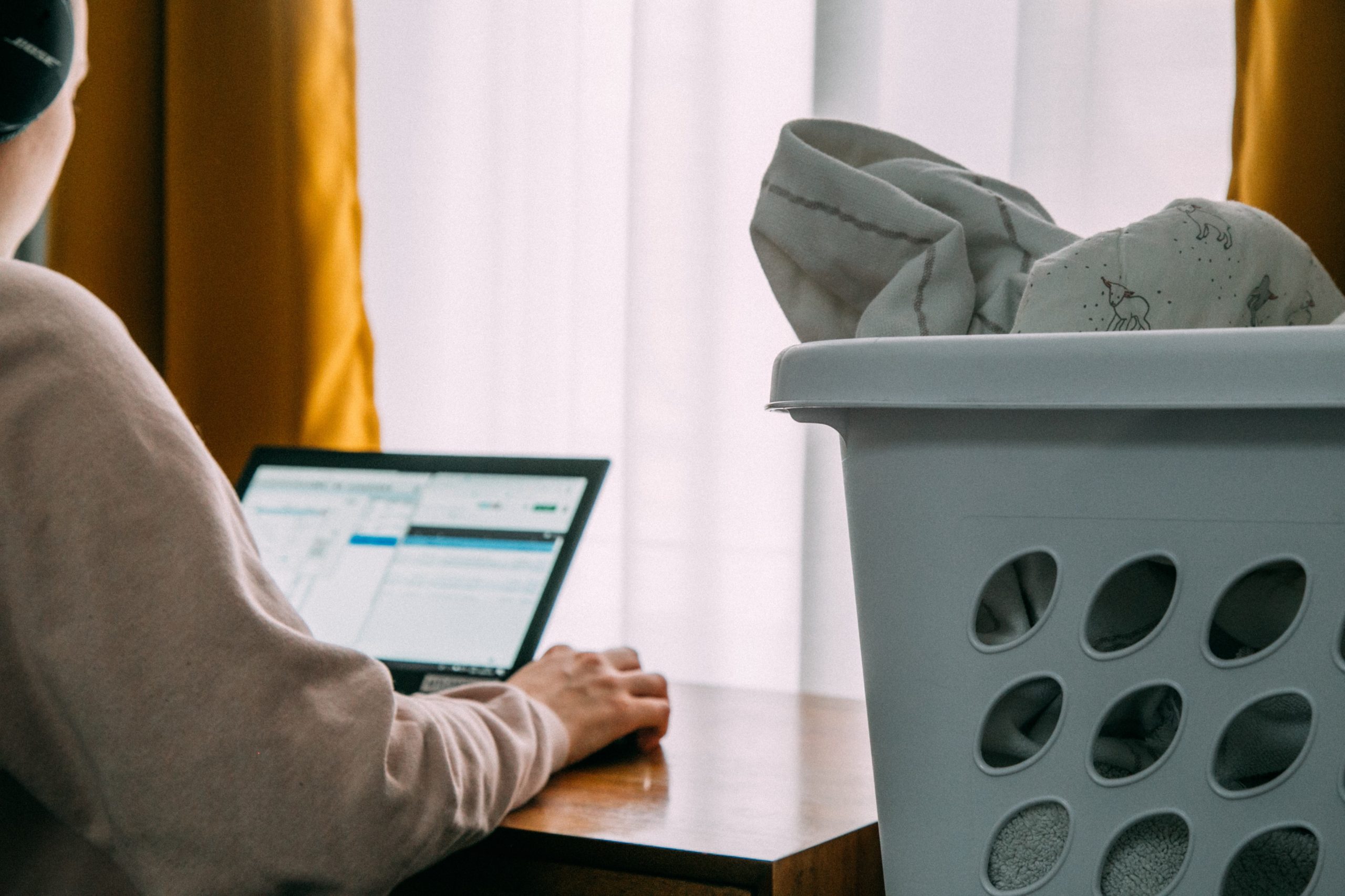 Image of person in grey hoodie working on laptop next to laundry basket