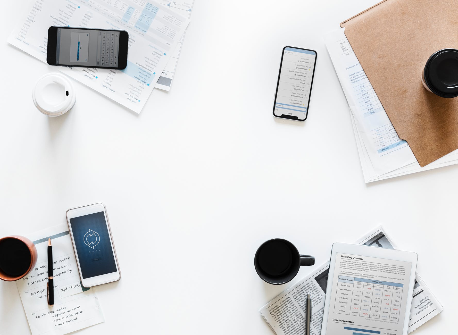 Growing Your Brand's Social Media Team featured image: smartphones and tablets and notepads and files with digital marketing topics on them, sitting near coffee mugs, spread out on a white table.