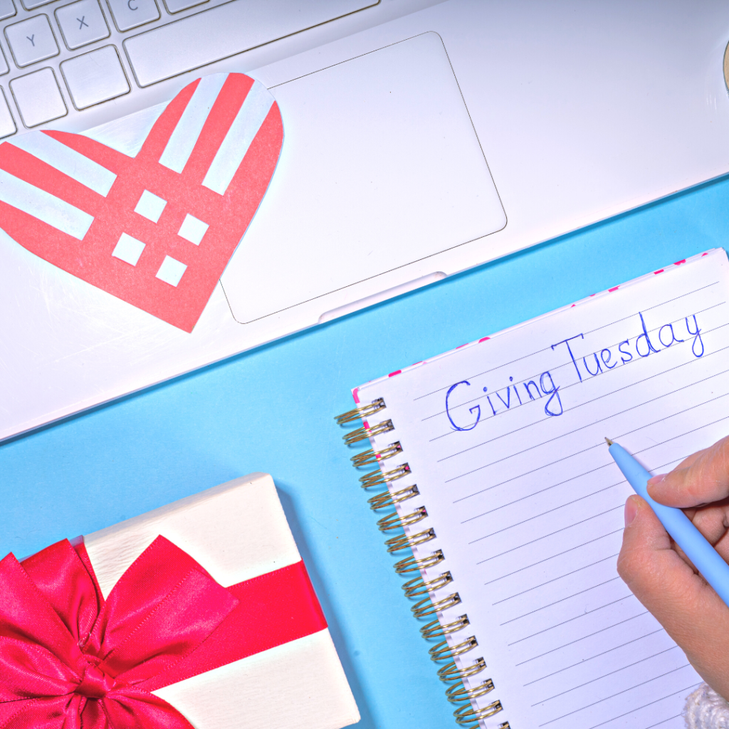 Giving Tuesday header image: hand holding pen over a notebook with "Giving Tuesday" written on it, next to a present box and a laptop with the official Giving Tuesday heart logo on it.