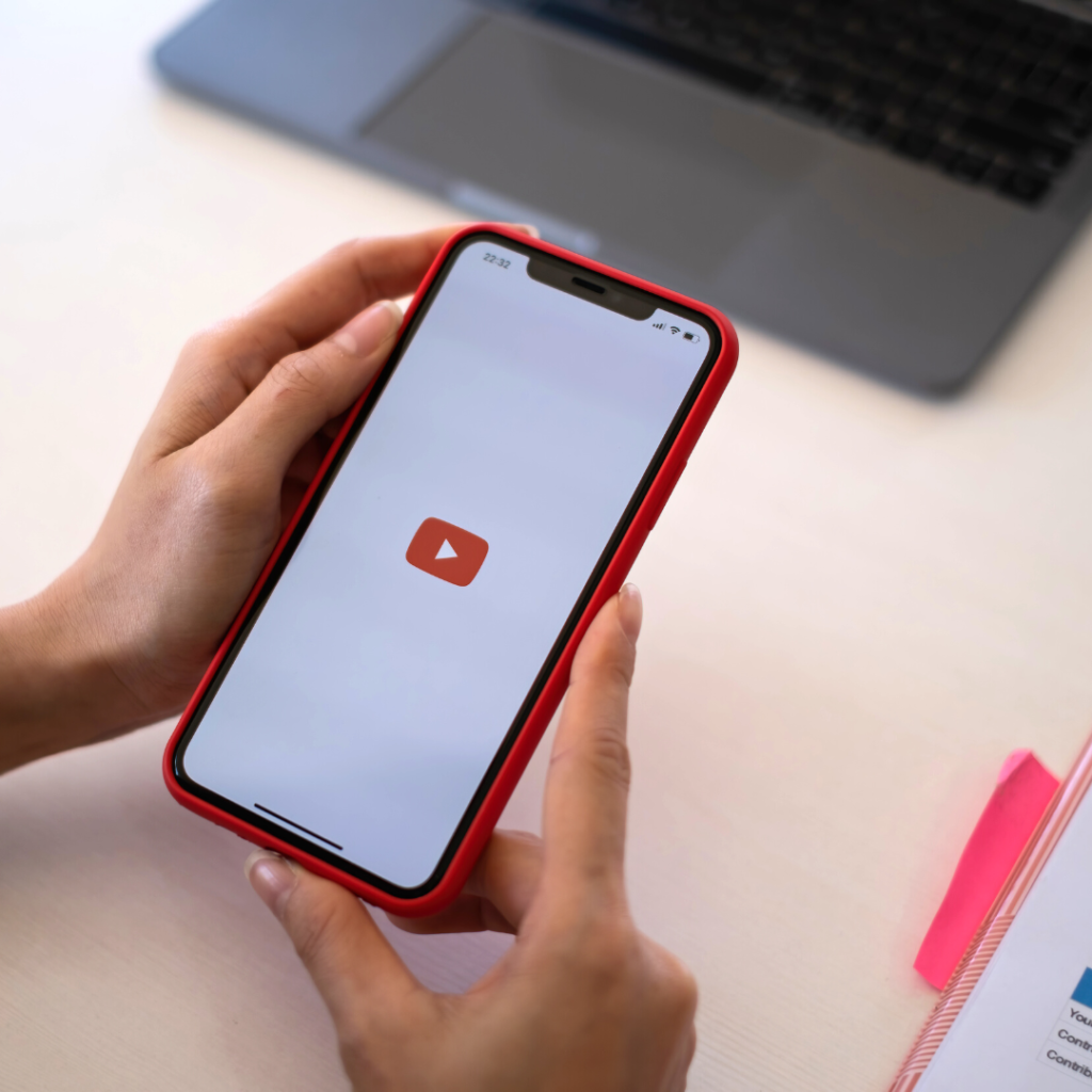 "A Simple Guide To Launching Shorts" blog featured image: hands holding a smartphone with the YouTube logo on its screen.