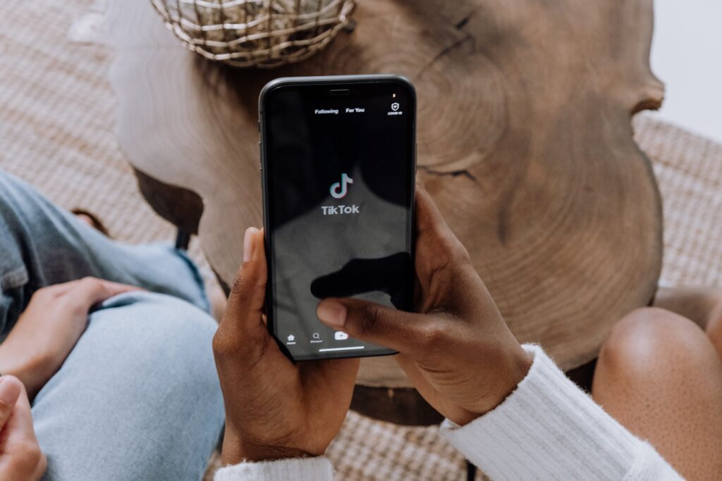"Simple Guide For Launching TikTok: Part 1" blog featured image: person in a white sweater holding a smartphone open to TikTok in their living room.
